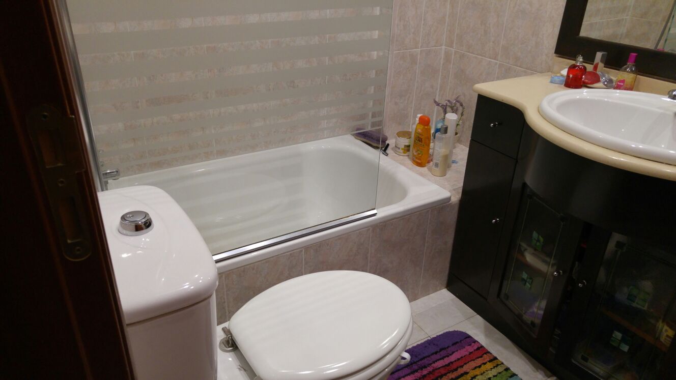 Baño antes de la reforma: bañera con media mampara junto al lavabo