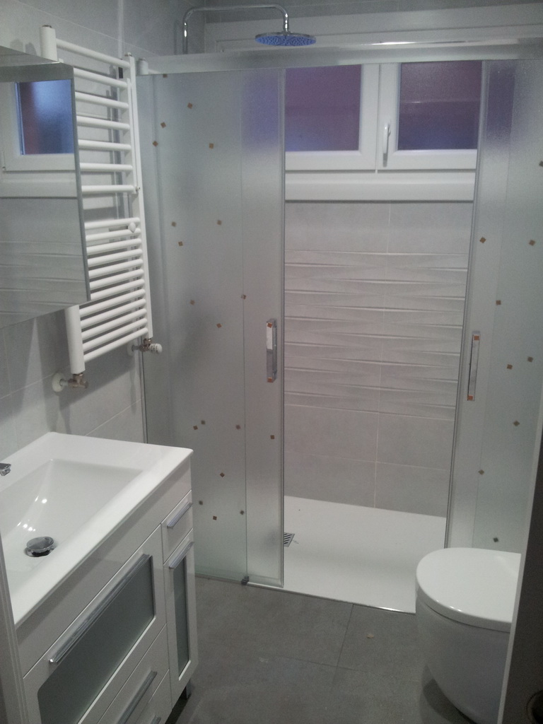 Baño gris con plato de ducha grande, mamparas correderas y toallero radiador